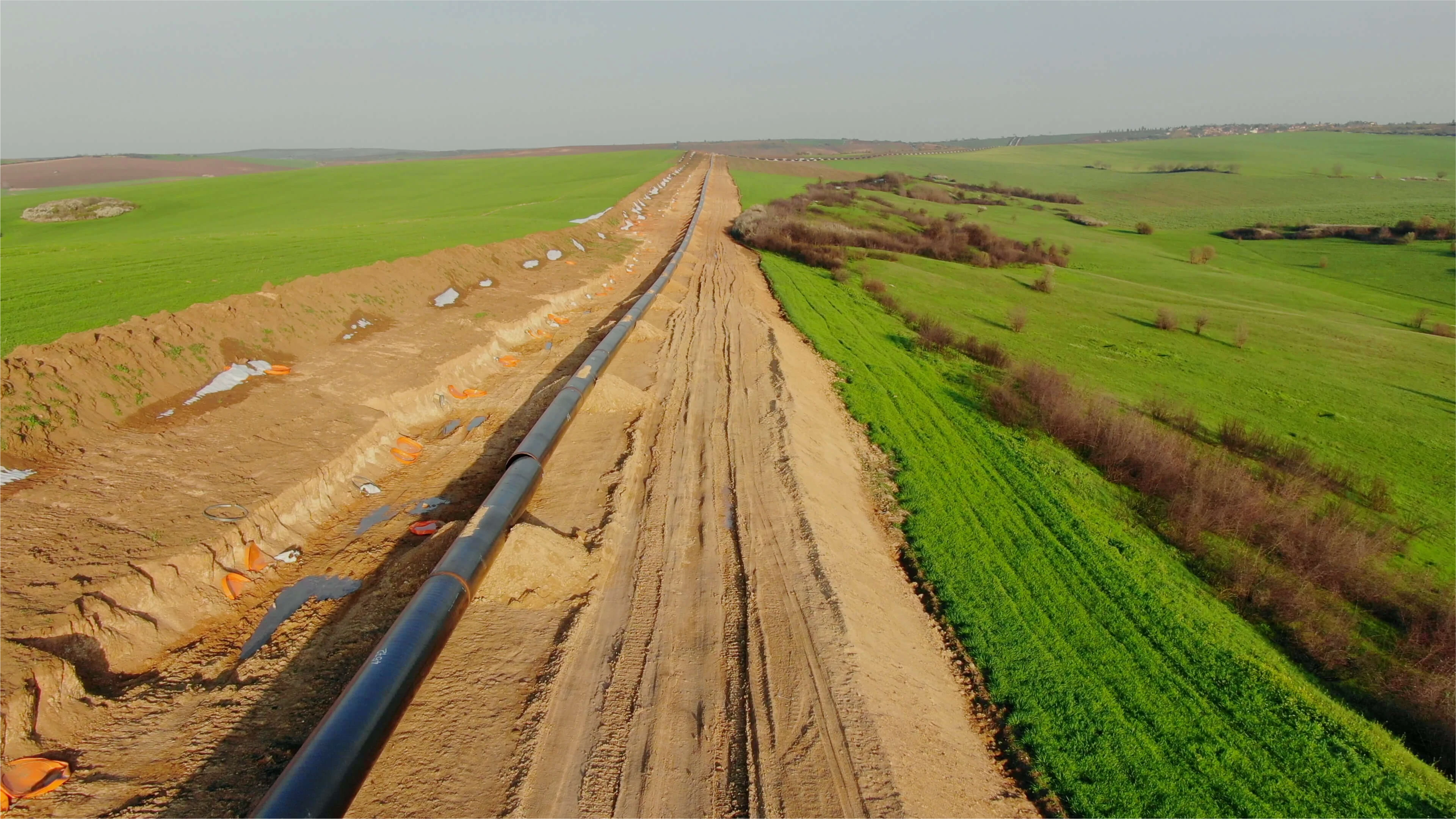 Aerial view of pipeline construction site with newly laid pipe through agricultural land, showing cleared dirt path alongside green fields