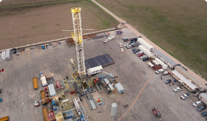 Aerial view of oil drilling rig site with equipment, vehicles, and support facilities on industrial lot